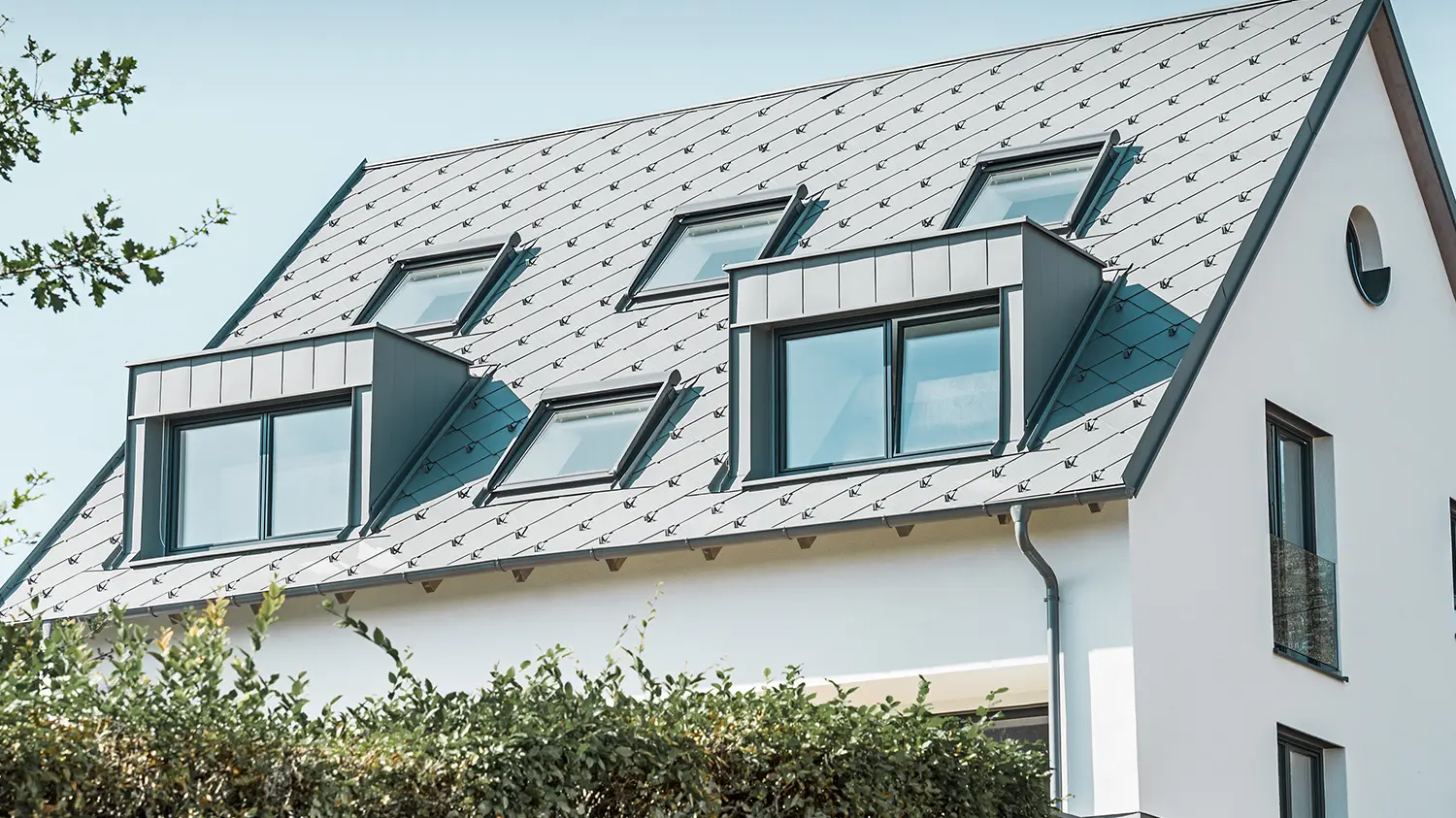 Rénovation d’un toit à deux pans avec deux lucarnes et quatre fenêtres de toit ; la toiture a été recouverte de losanges de toiture 44 × 44 PREFA couleur gris souris. Le choix s’est porté sur une gouttière suspendue PREFA également couleur gris souris. 