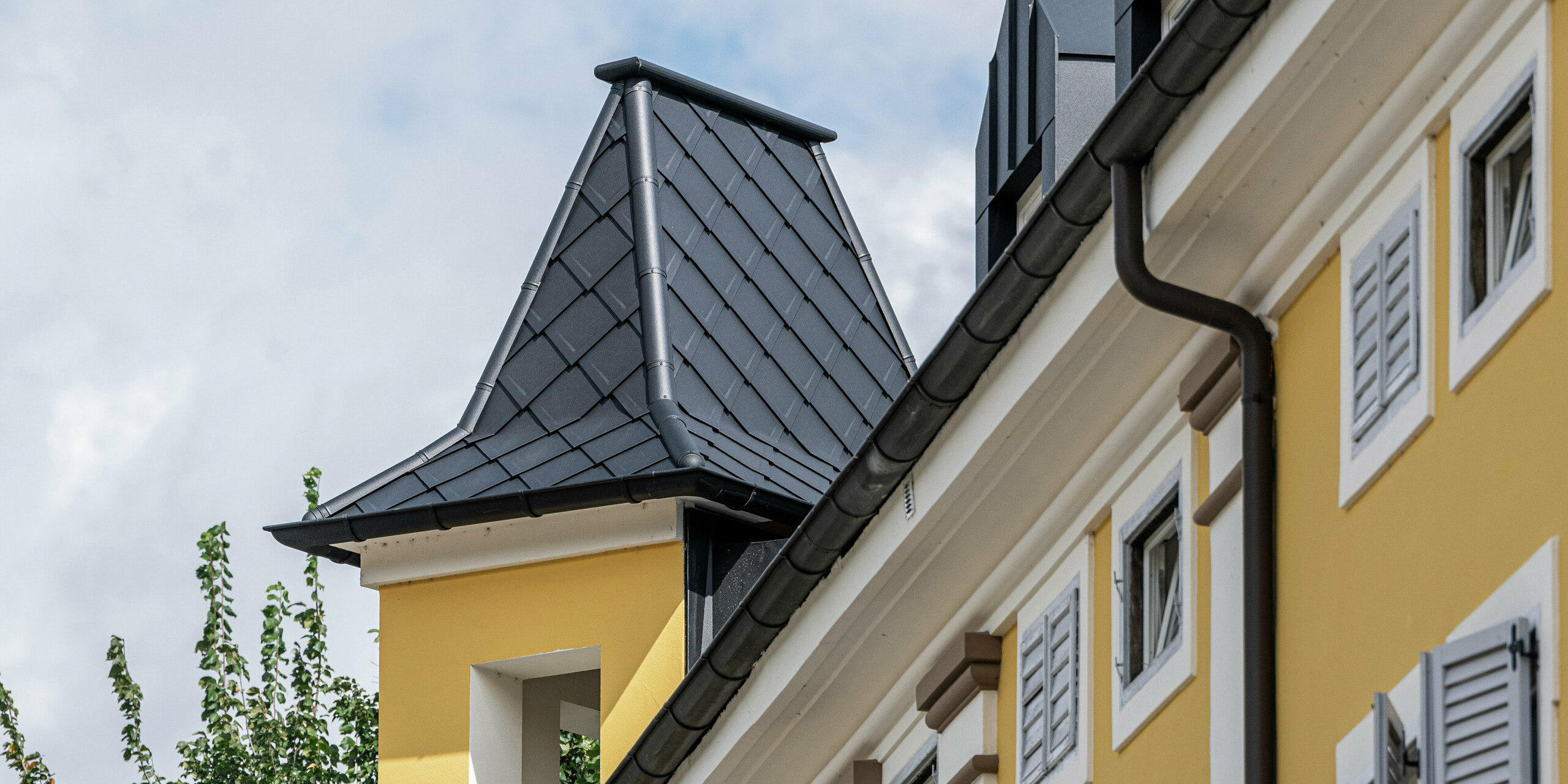 Vue détaillée de la tour historique de l'hôtel Jarolim à Bressanone, conçue avec des losanges en aluminium PREFA. Les produits PREFA, résistants aux intempéries et légers, préservent le caractère historique du bâtiment et garantissent une solution de toiture durable et esthétique. La finition de haute qualité des lucarnes et du revêtement de la tour souligne la combinaison de l'architecture traditionnelle et de la technologie moderne - idéale pour les bâtiments classés.