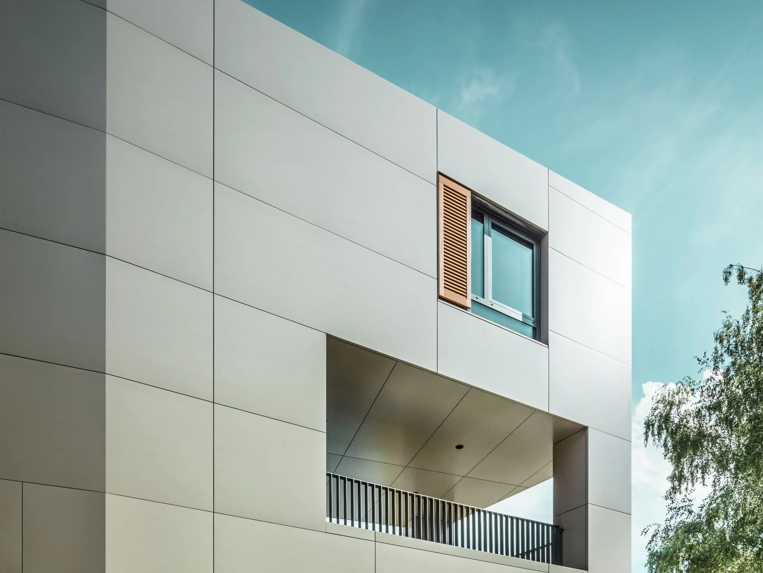 La photo montre la mairie moderne d'Alzenau avec une façade en panneaux composites en aluminium PREFA couleur bronze. L'architecture se caractérise par des formes géométriques claires et de grandes fenêtres. La toiture pointue et l'éclairage discret confèrent au bâtiment un aspect élégant et contemporain.