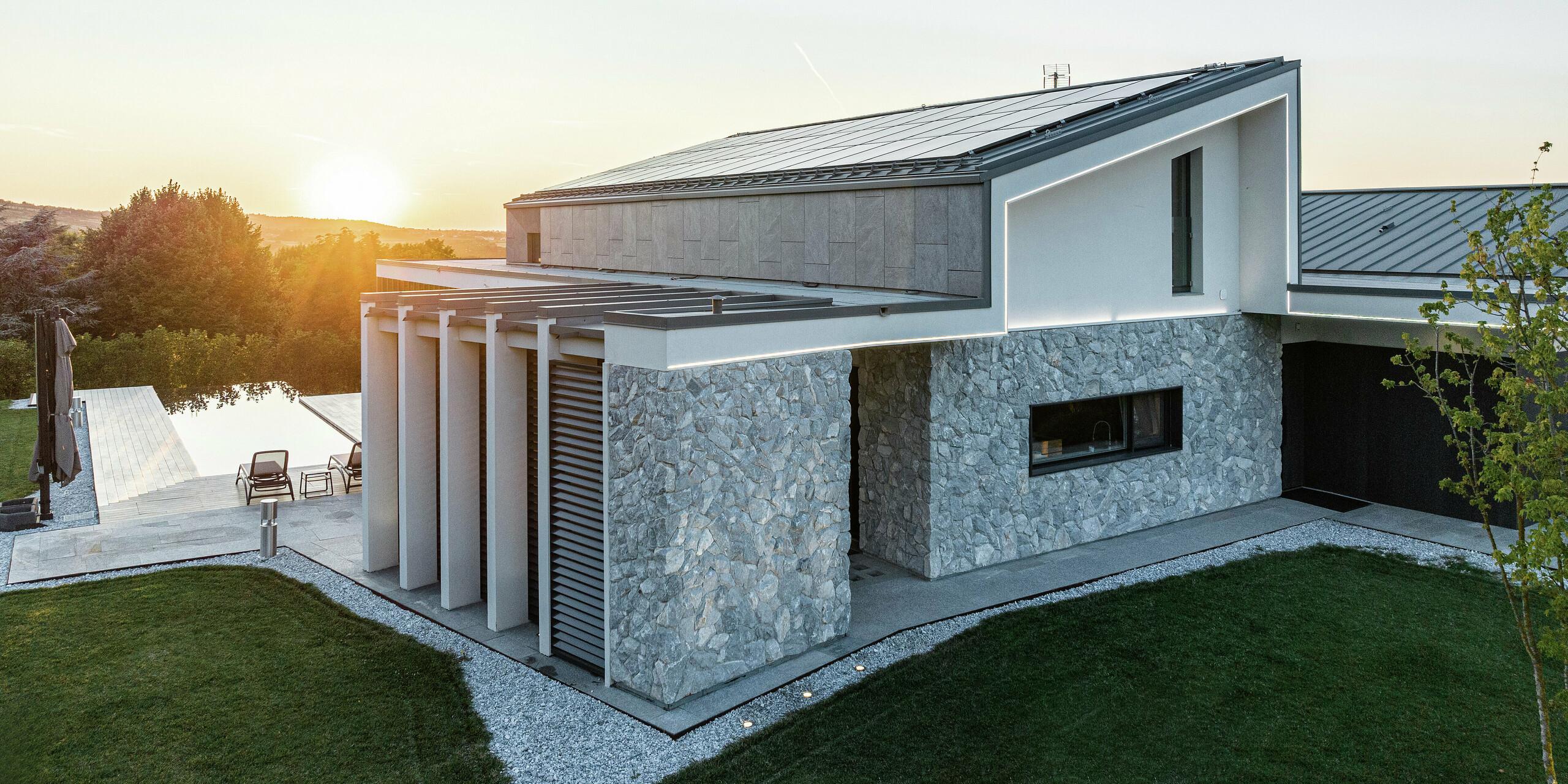 Detailansicht des luxuriösen Einfamilienhauses in Scandiano, Italien. Die Dachflächen aus PREFALZ in P.10 Anthrazit sorgen für ein modernes, elegantes Erscheinungsbild und bieten optimalen Witterungsschutz. Die Natursteinfassade und die klaren Linien des Designs harmonieren perfekt mit der hochwertigen PREFA Dachlösung und der durchdachten Architektur.