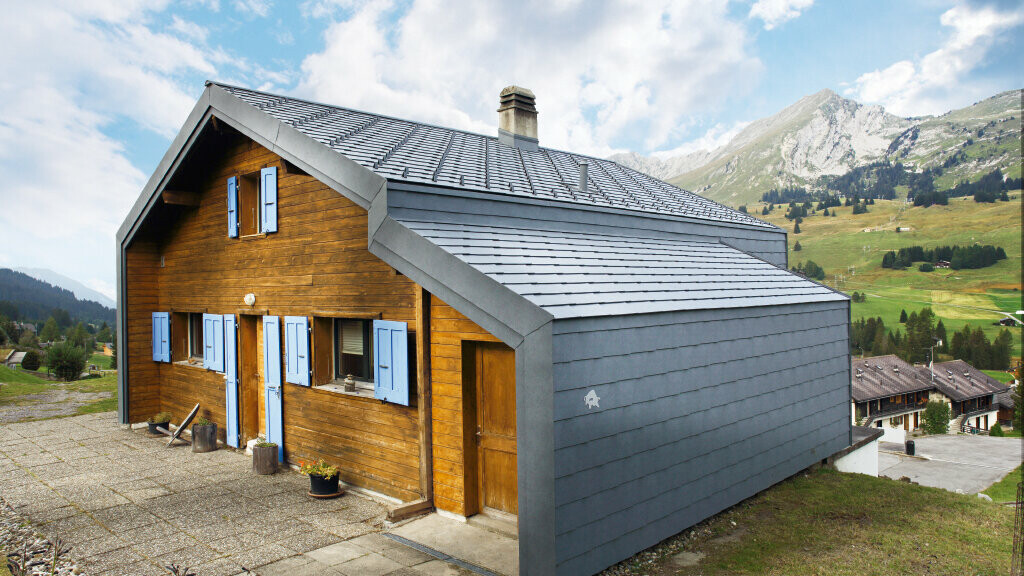 Maison dans les montagnes suisses avec façade en bois, combinée au losange de toiture et de façade PREFA couleur gris pierre