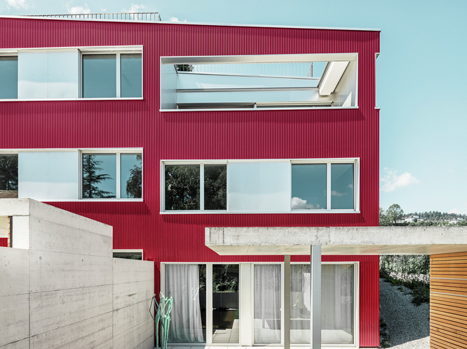 Vorderansicht eines Wohnhauses am Zürichsee in der Schweiz bei Sonnenschein und blauem Himmel, verkleidet mit der PREFA Profilwelle in der Farbe Weinrot