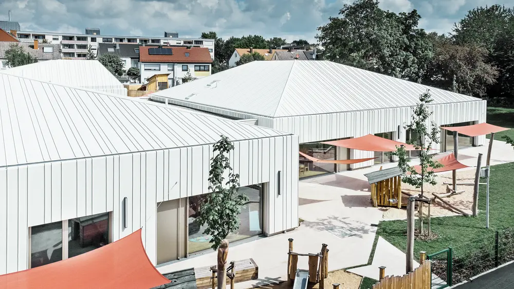 Nous pouvons apercevoir l'école maternelle de Niederwerrn qui a été recouverte avec le système de toit Prefalz de PREFA, avec un aperçu sur le jardin