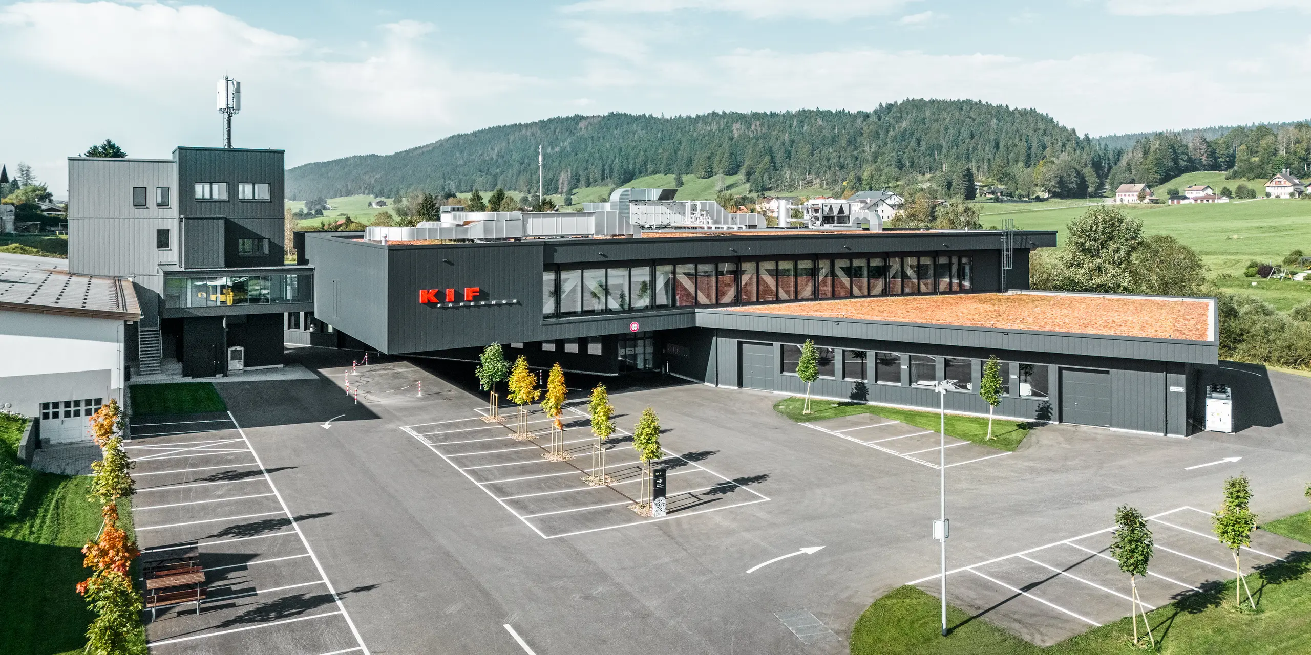 Luftaufnahme des Firmengebäudes von KIF Parechoc in Le Brassus: Die weitläufige Anlage fügt sich harmonisch in die grüne Hügellandschaft ein. Die Fassade mit PREFA Sidings in P.10 Anthrazit und Patinagrau betont die klare, moderne Architektur und die markanten Gebäudekanten. Das langlebige Aluminium überzeugt durch hohe Witterungsbeständigkeit, Korrosionsschutz und geringen Wartungsaufwand bei dauerhaft hochwertiger Optik.