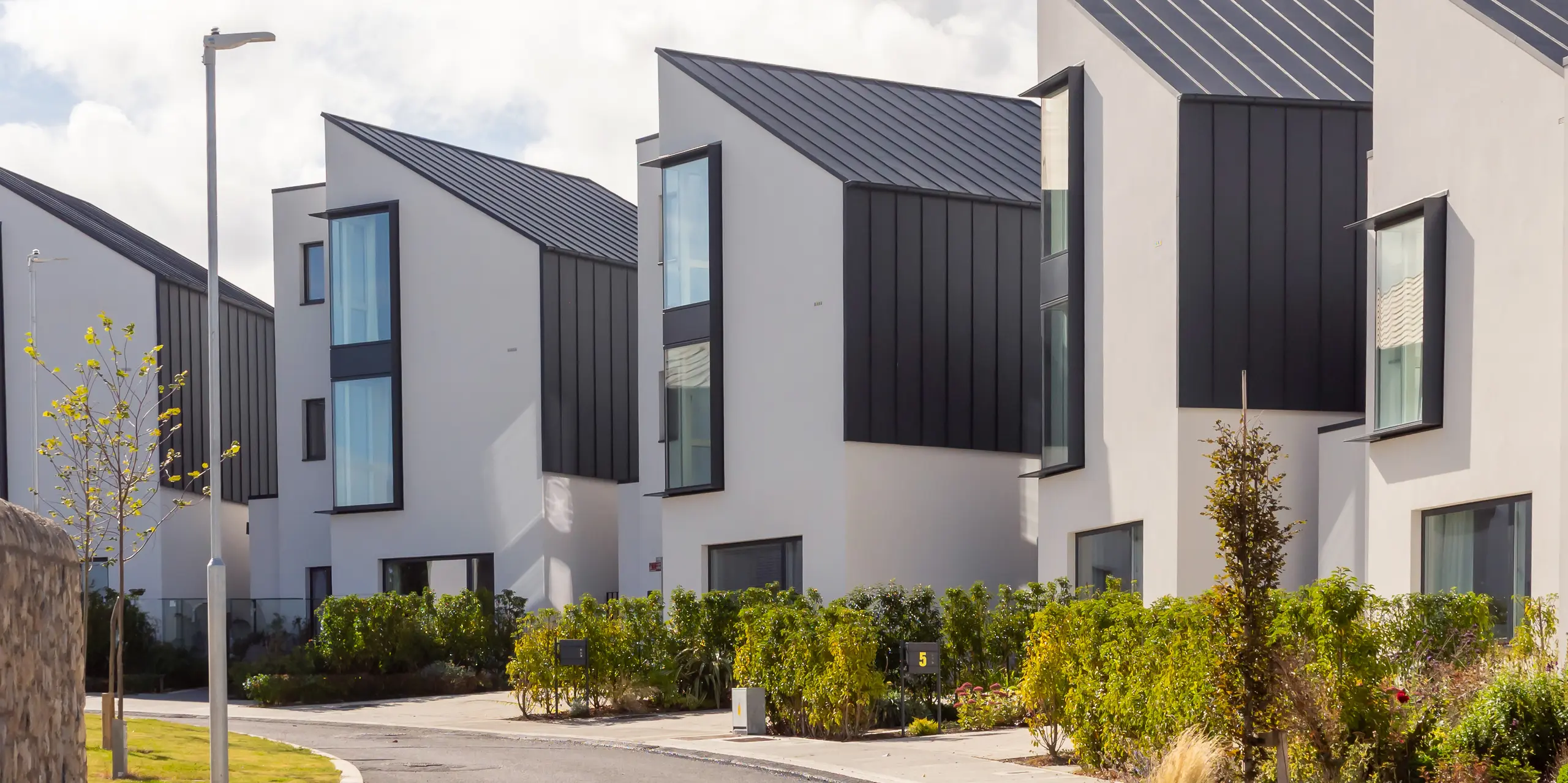 Le complexe résidentiel moderne Watson Place, près de Dublin, se distingue par ses toitures asymétriques épurées et son bardage PREFALZ P.10 anthracite. De larges baies vitrées et des surfaces en aluminium aux lignes affirmées soulignent le dynamisme de l'architecture. Les produits PREFA, résistants et durables, assurent une protection efficace contre les intempéries et confèrent au complexe une allure élégante et haut de gamme.