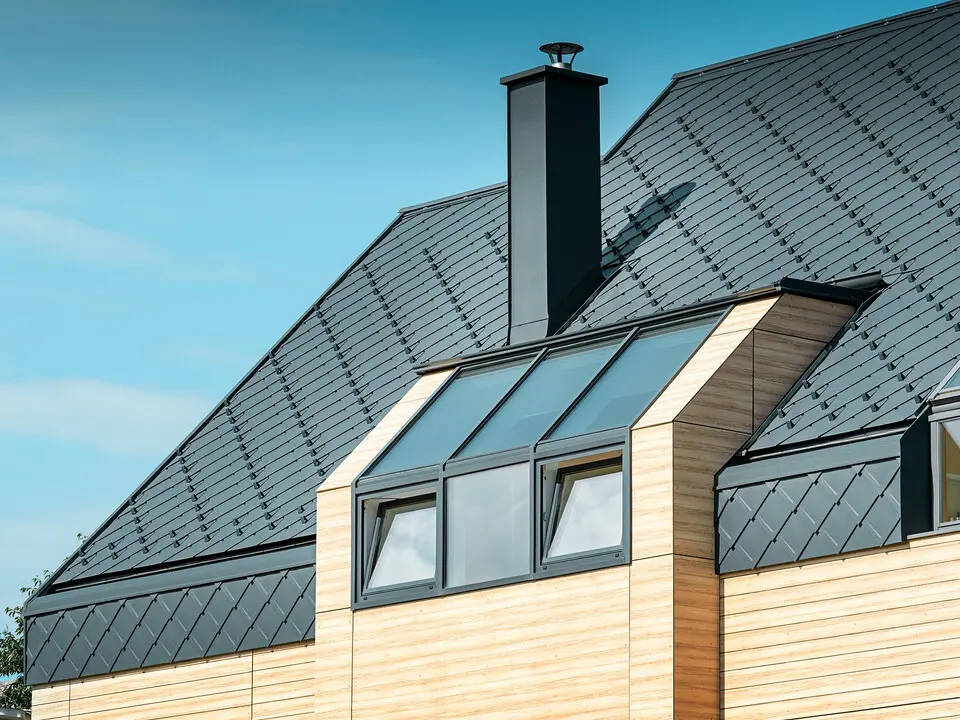 Maison individuelle au toit à deux versants sans saillie de toit — Façade à l’aspect du bois et toiture en aluminium PREFA de couleur anthracite