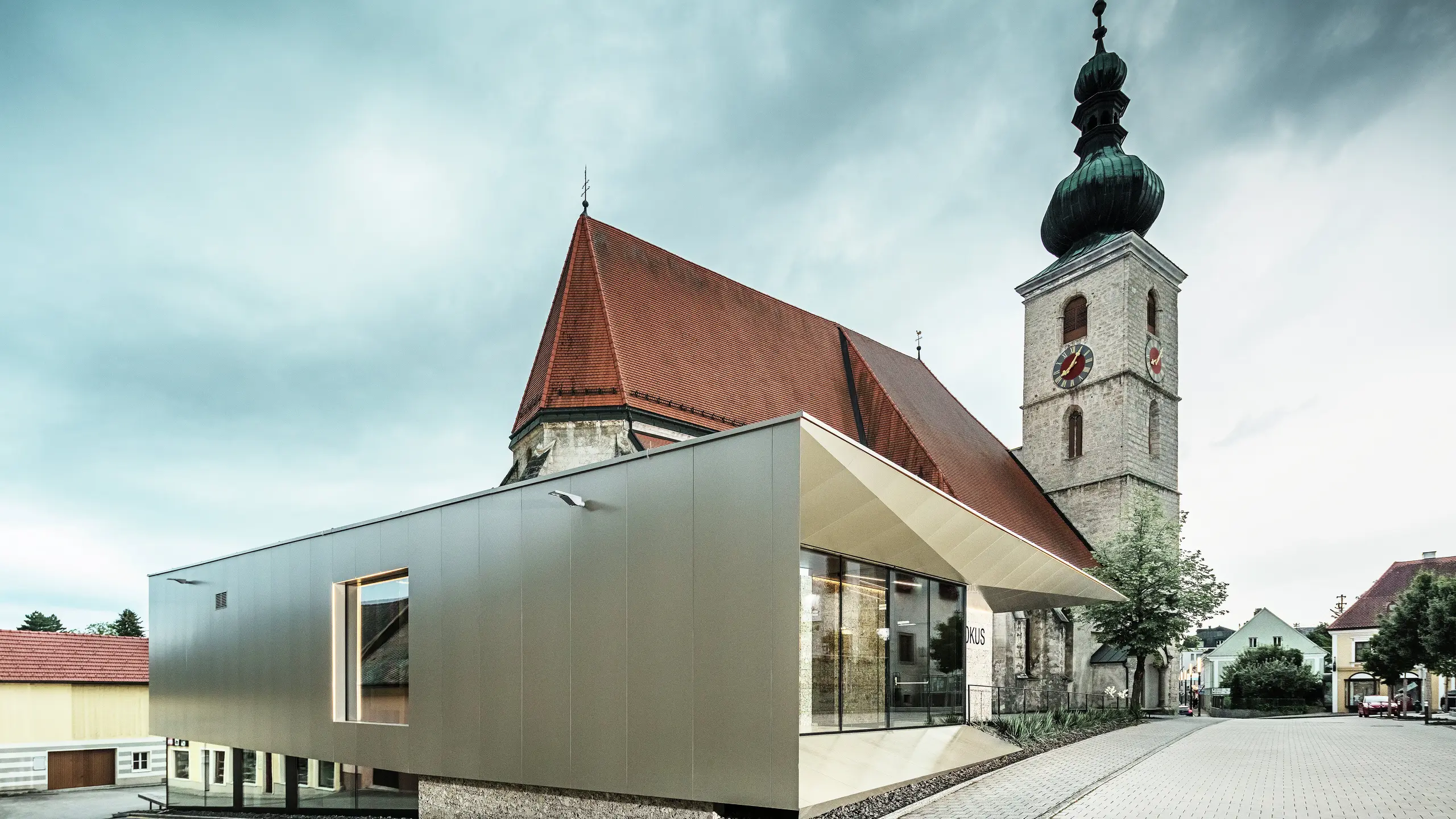 La vue latérale montre l'avant-toit filigrane, réalisé avec des panneaux composites en aluminium PREFA de haute qualité. La finition précise confère un aspect moderne aux lignes épurées et souligne le lien architectural entre l'ancien et le nouveau.