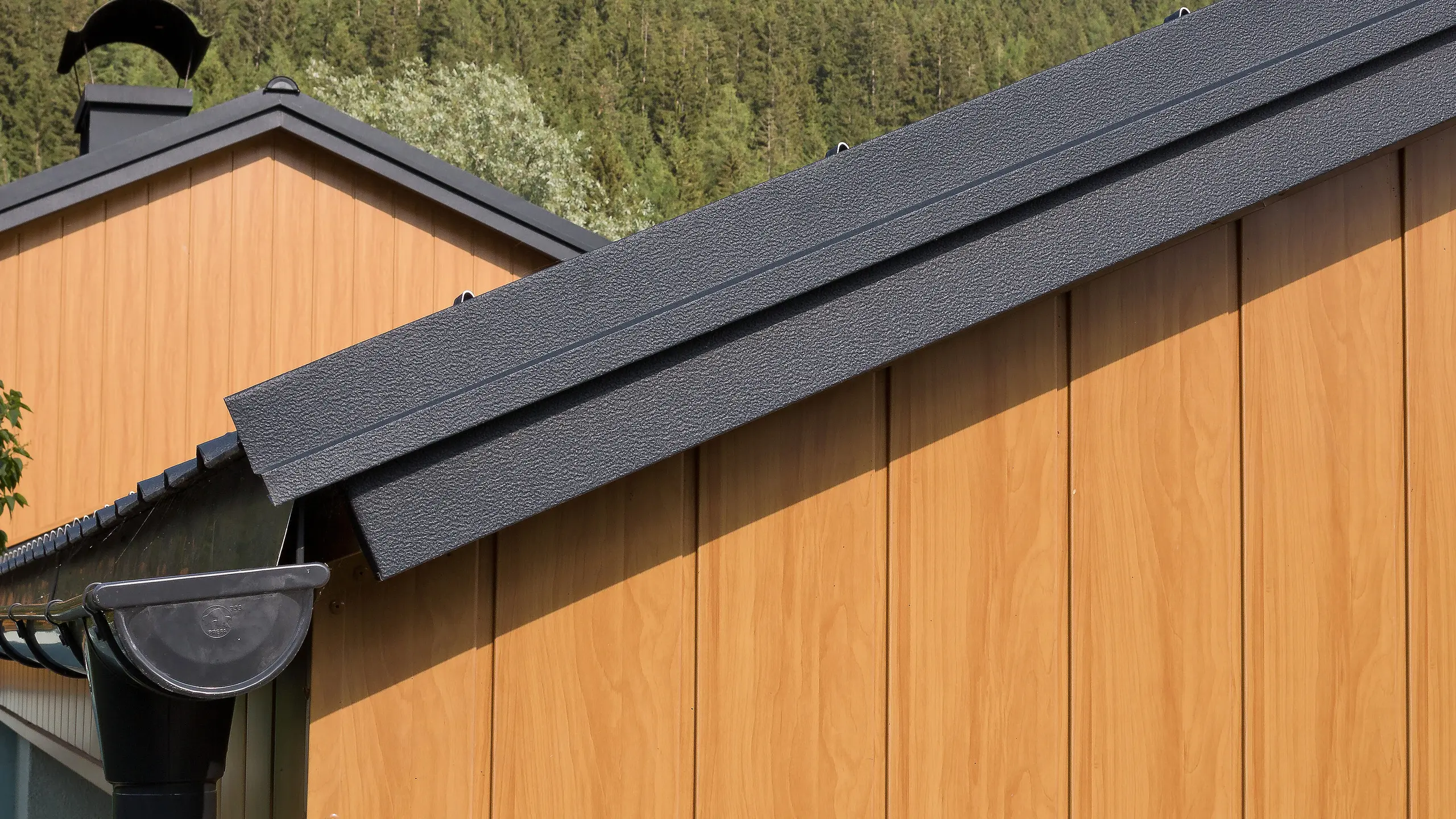 Revêtement de pignon avec les Sidings en aluminium de PREFA couleur chêne naturel montés à la verticale avec une gouttière PREFA anthracite.