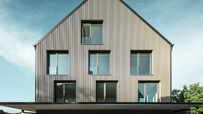La photo montre un bâtiment moderne à Feldkirchen, conçu par l'architecte Stefan Heigl. La façade est recouverte de Prefalz de couleur bronze, tandis que le toit à pignon est recouvert de Prefalz de couleur gris noir. De grandes fenêtres rectangulaires laissent entrer beaucoup de lumière naturelle à l'intérieur. Le bâtiment allie des matériaux de haute qualité et une architecture élégante, à la fois fonctionnelle et esthétique. Cette construction moderne et l'utilisation de matériaux Prefalz confèrent au bâtiment un aspect contemporain et élégant.