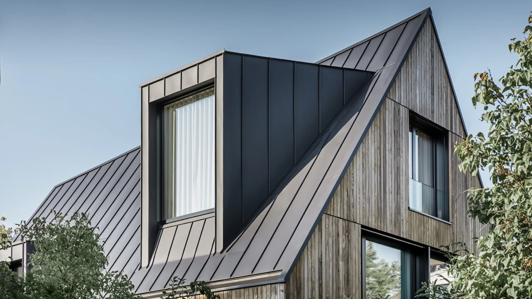 Toit à pignon raide avec grande lucarne, recouvert avec PREFALZ de PREFA en anthracite et joints debout du toit combinés avec la façade en bois