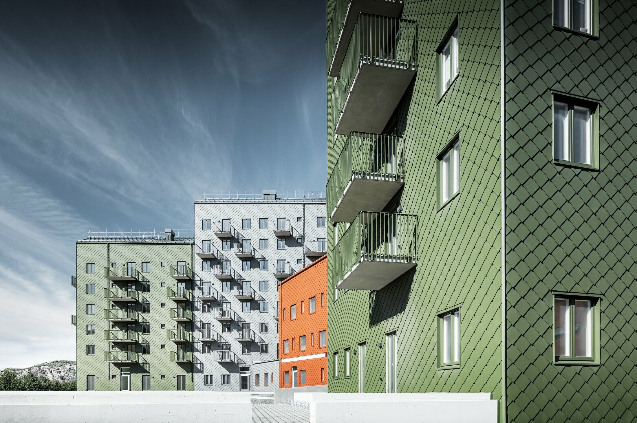 Plusieurs bâtiments d’habitation les uns à côté des autres, recouverts de losanges de façade 29 × 29 PREFA dans les teintes rouge tuile, vert olive et gris souris.