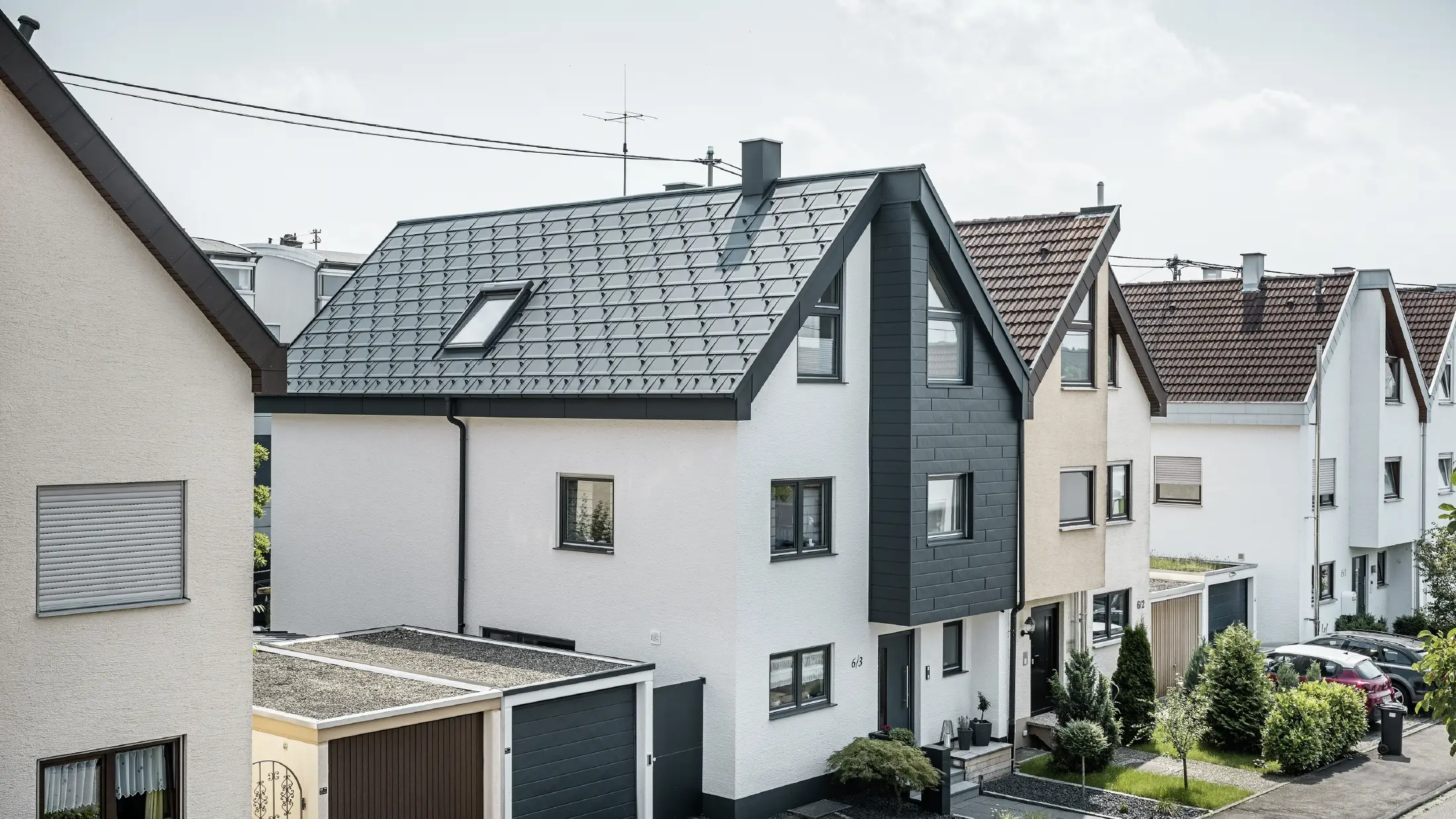 La moitié d'une maison jumelée a déjà été rénovée, avec une façade fraîchement crépie de blanc, combinée à une façade avec Siding.X PREFA en anthracite. Le toit est recouvert du R.16 PREFA. L'écoulement des eaux de pluie se fait par la gouttière carrée et le tuyau de descente PREFA.