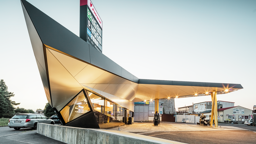 Vue latérale de la station-service dynamique, habillée d'aluminium, conçue par l'architecte Daniel Zerzán : la façade est structurée par plusieurs triangles et trapèzes.