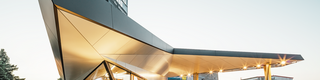 Vue latérale de la station-service dynamique, habillée d'aluminium, conçue par l'architecte Daniel Zerzán : la façade est structurée par plusieurs triangles et trapèzes.