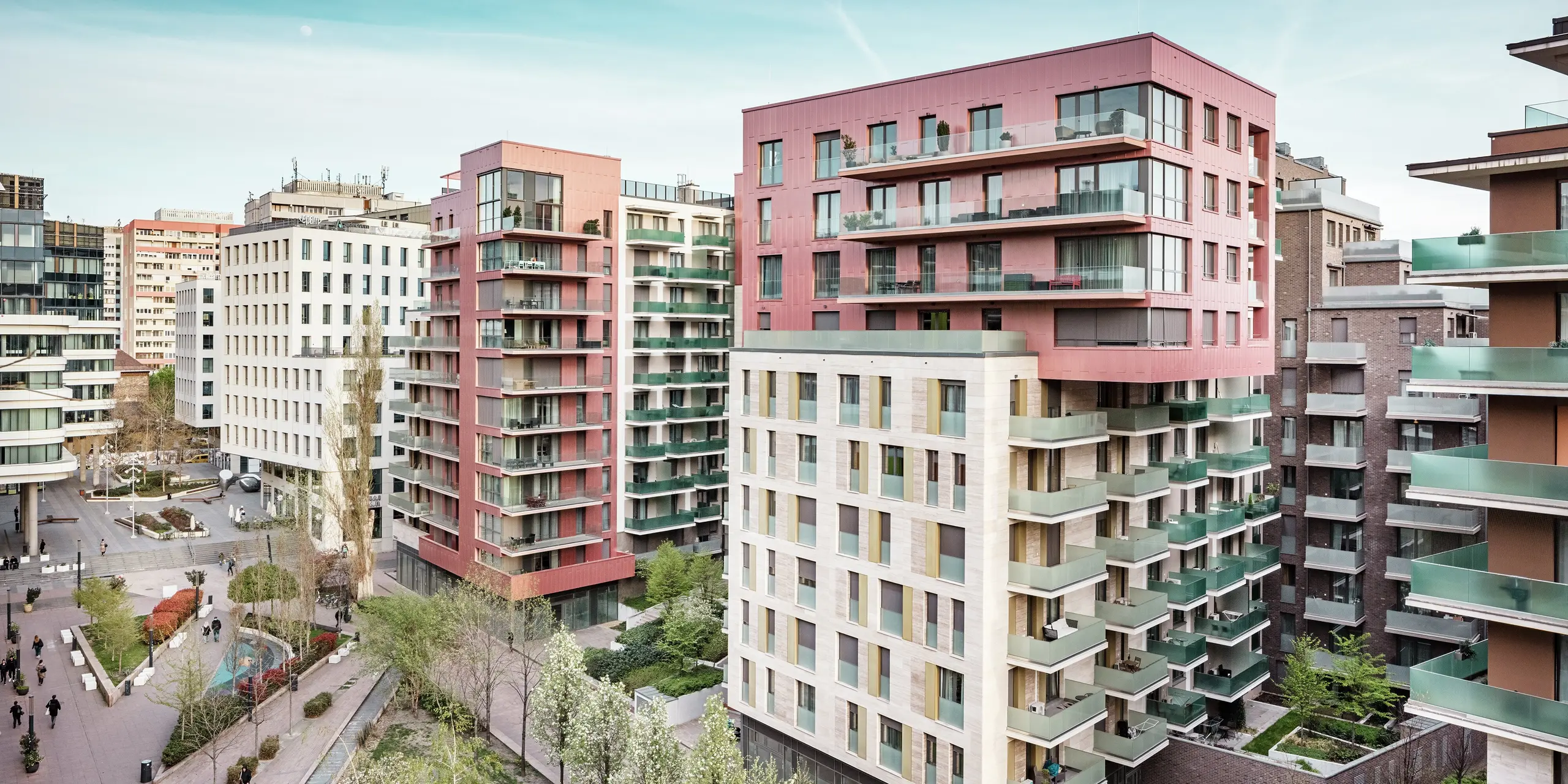 Vue d'ensemble saisissante du Grand Corvin Ensemble, dans le quartier Corvin de Budapest. Les étages supérieurs, remarquables, sont conçus avec des panneaux de façade Siding PREFA, posés verticalement et finis dans une couleur métallisé saumon spéciale. Associés à la pierre naturelle et à de généreuses surfaces vitrées, ils créent un paysage urbain moderne et de grande qualité. La façade en aluminium durable souligne la diversité architecturale et les aspirations durables de ce projet de rénovation urbaine globale.