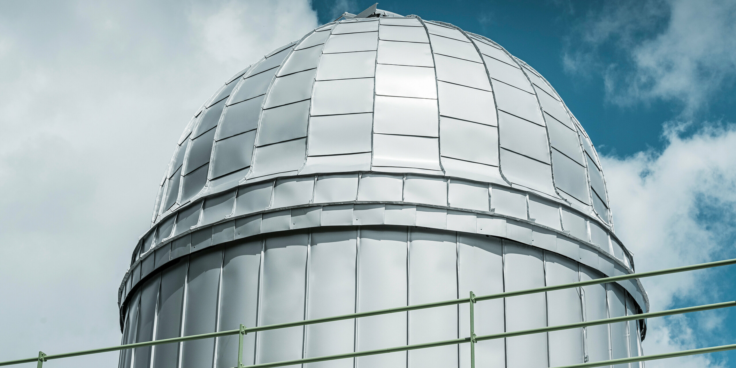 Detailní pohled na sálavou kopuli Hvězdárny na Skalnatém Plese, pokrytou PREFALZ ve stříbrné metalíze. Lesklý hliníkový plášť odráží modrou oblohu a symbolizuje odolnost vůči náročným klimatickým podmínkám v nadmořské výšce 1 783 metrů.