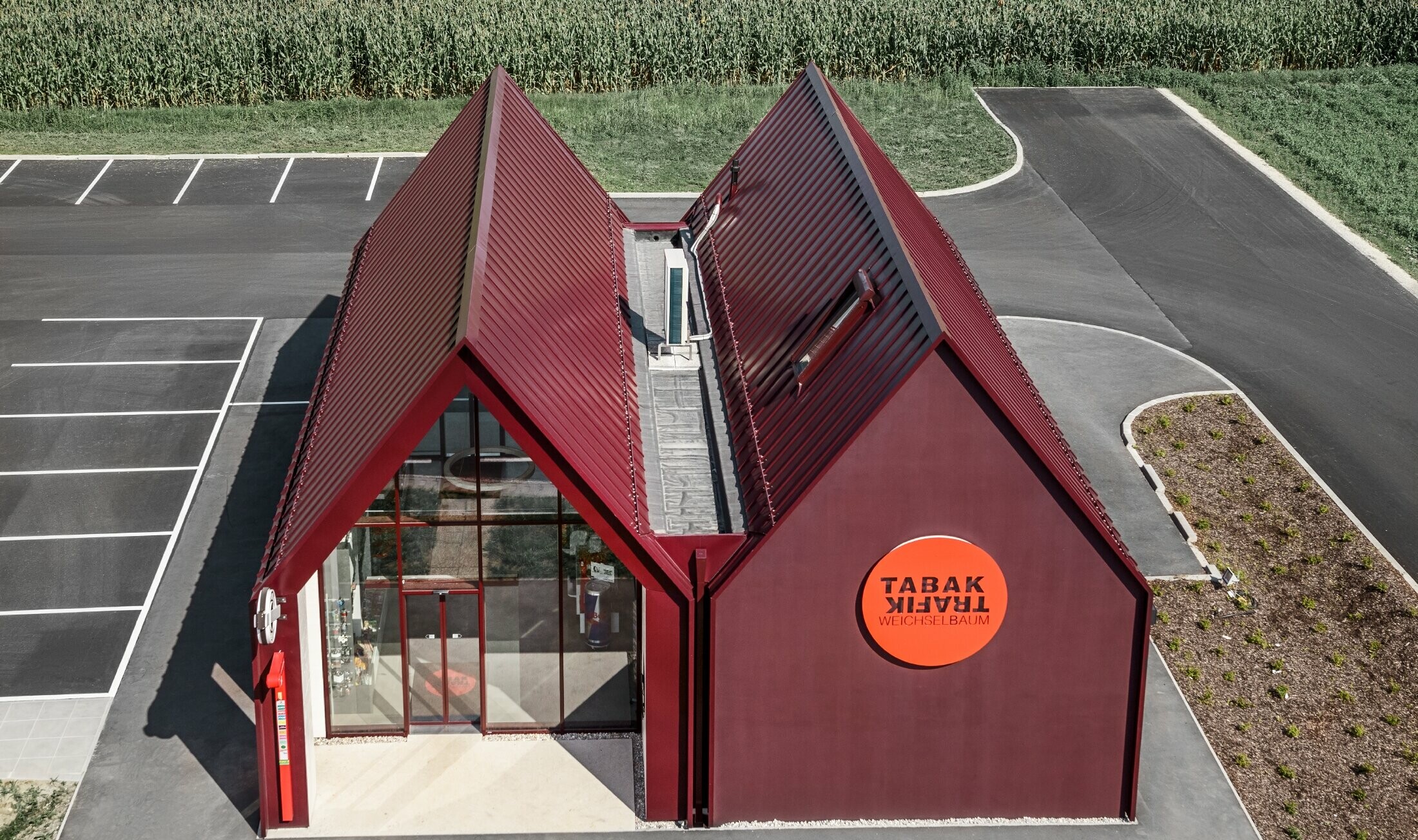 Bureau de tabac moderne au toit à deux versants sans saillie de façade — Enveloppe en aluminium PREFA à joints debout et joints angulaires rouge-noir (couleur spéciale)