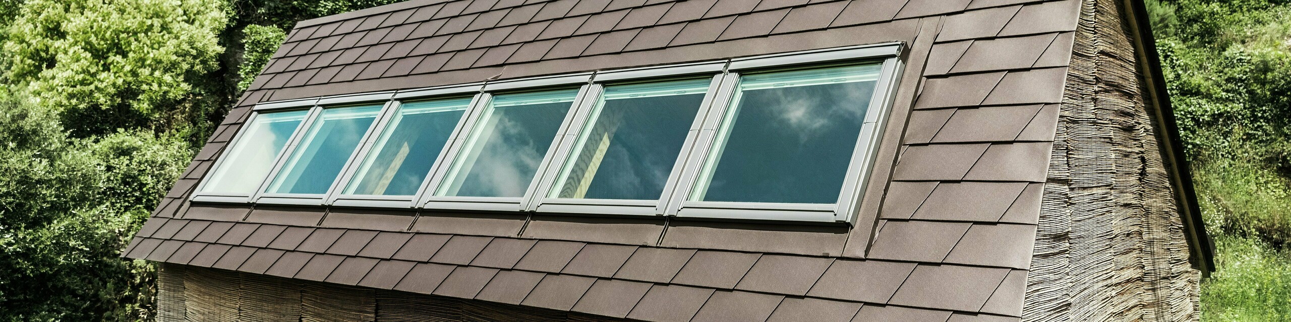 Bardeaux de toiture PREFA de couleur P.10 brun noisette sur le toit d'une maison moderne avec puits de lumière - une solution en aluminium durable pour l'efficacité énergétique et une conception de toit élégante.