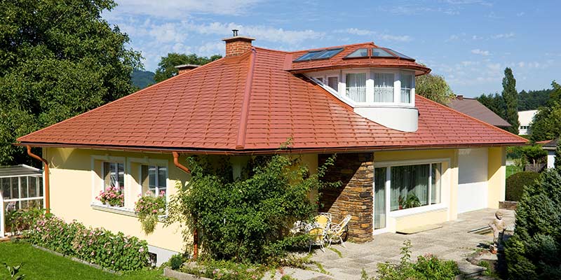 Maison individuelle avec toit à croupes et lucarne recouverte avec le bardeau PREFA en aluminium imitation tuile, rouge tuile.