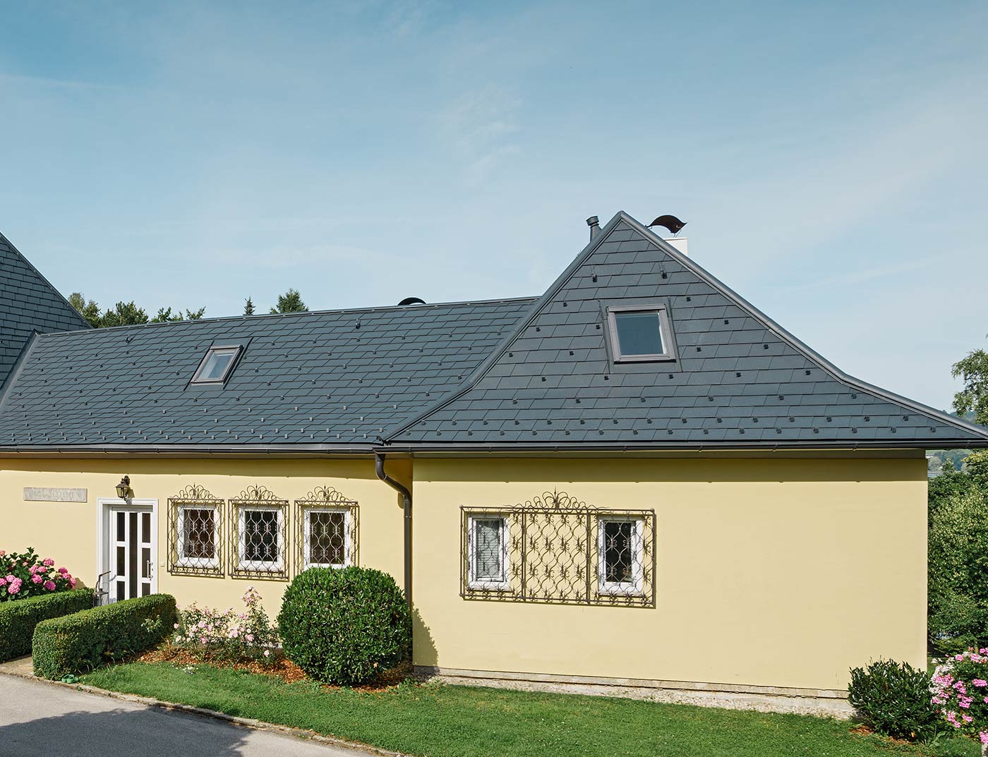 Maison individuelle avec toit en croupe et façade en plâtre jaune; Le toit á été recouvert de bardeau anthracite PREFA.